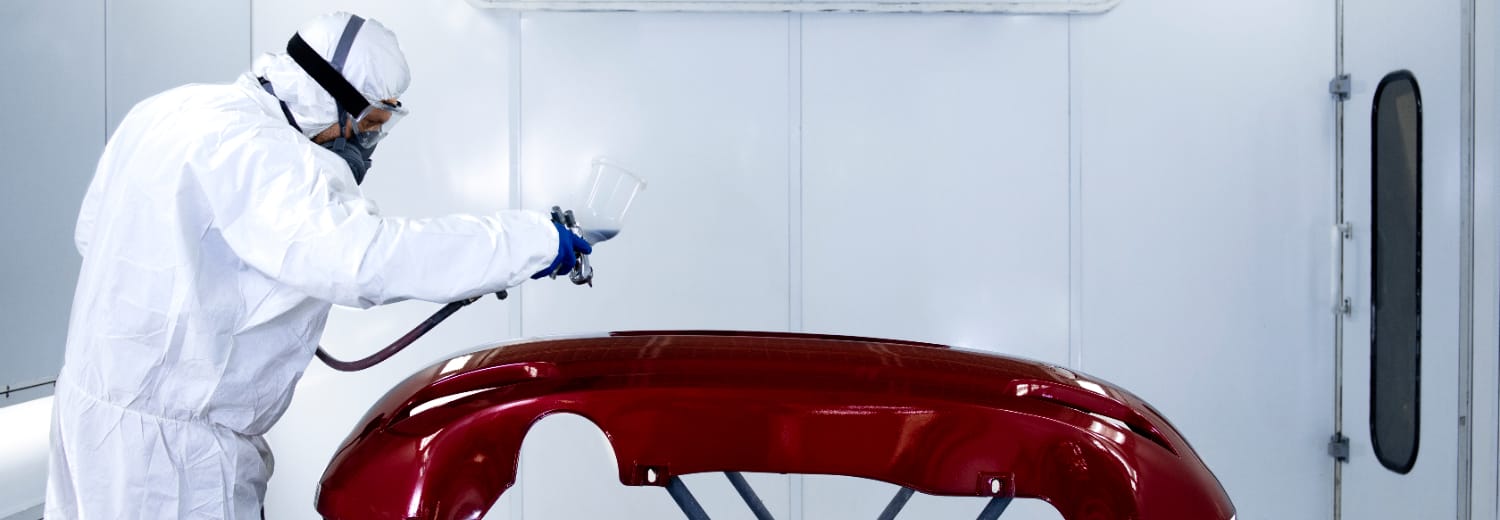 Inspeção final em peça automotiva recém-pintada. Ambiente iluminado e fechado, ideal para acabamento e controle visual de qualidade. Operador com EPI e em posição técnica de análise. Condições adequadas de luminosidade e limpeza observadas.