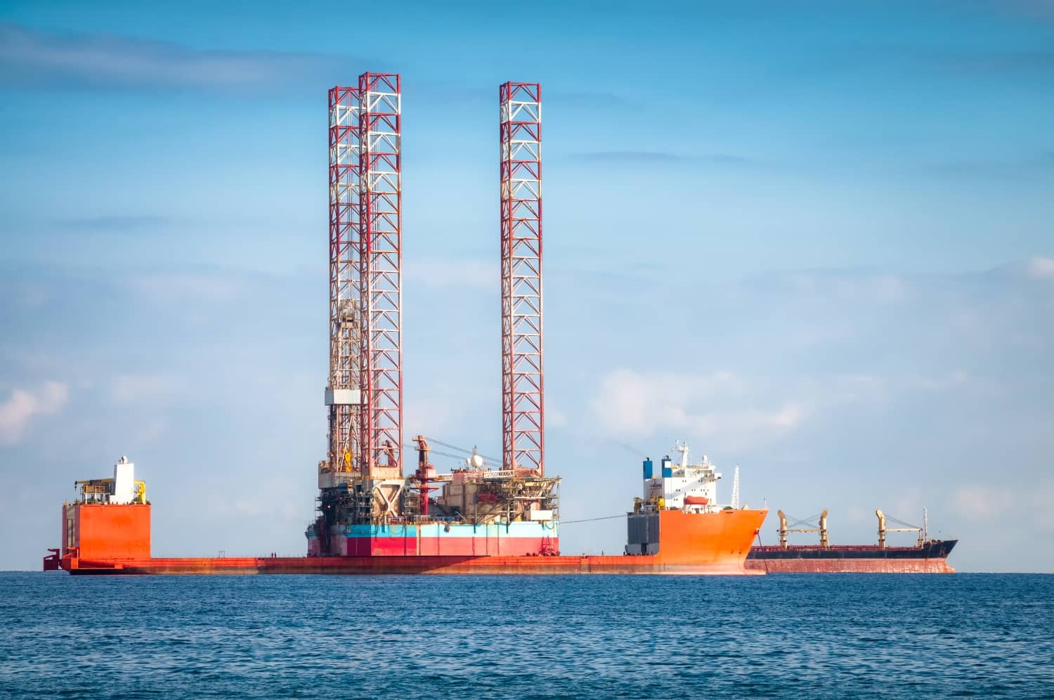Unidade autoelevatória (Jack-Up) posicionada para operação de perfuração, com apoio logístico de embarcação de suprimentos no ambiente offshore. - Curso NR 37 - Nível Avançado.