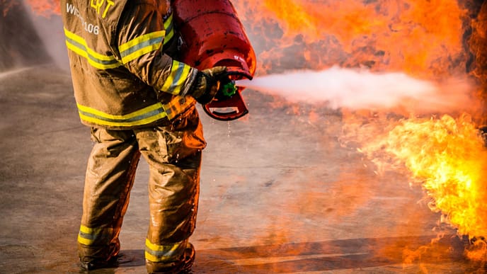 Seção baixa de bombeiro pulverizando extintor em chamas. - Consultoria NR 23