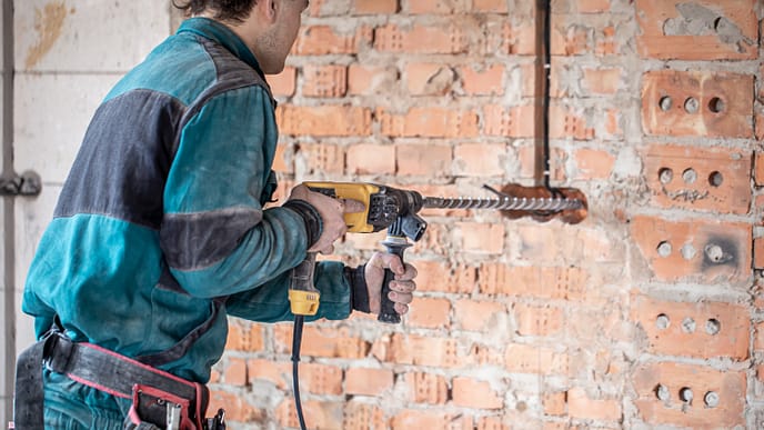 Técnico utilizando uma furadeira de impacto com broca SDS para perfuração de uma parede de tijolos, ferramenta essencial para trabalhos em alvenaria e concreto. - Curso Furadeira e Rosqueadeira.